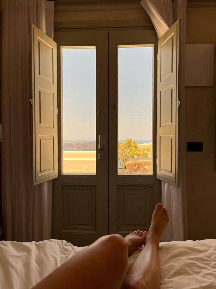 Enjoy a serene view from a bedroom in Fira, Greece with open doors and a beautiful landscape.